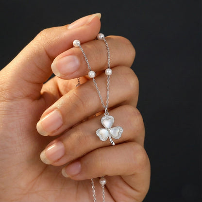 Hand holding a silver necklace with a clover-shaped pendant against a dark background