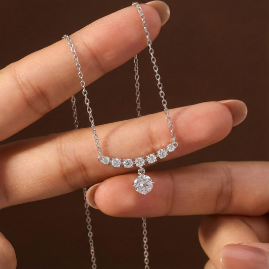 Silver necklace with a pendant held between fingers against a brown background