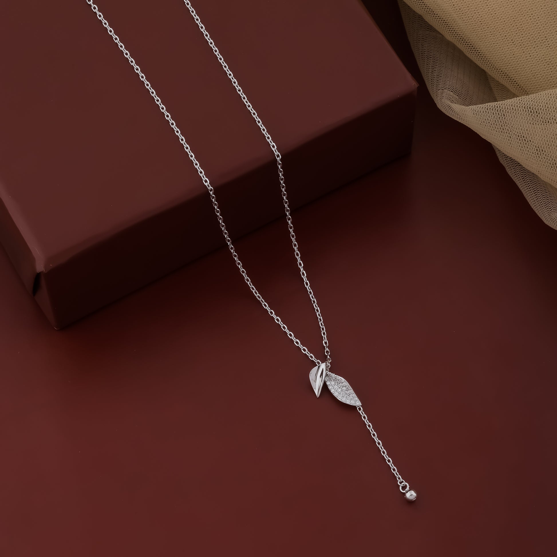 Silver necklace with a leaf pendant on a dark brown surface