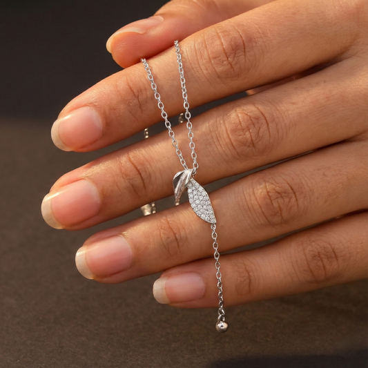 Silver necklace with leaf pendant on a hand against a brown background