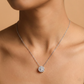 Silver necklace with a diamond pendant on a model against a beige background