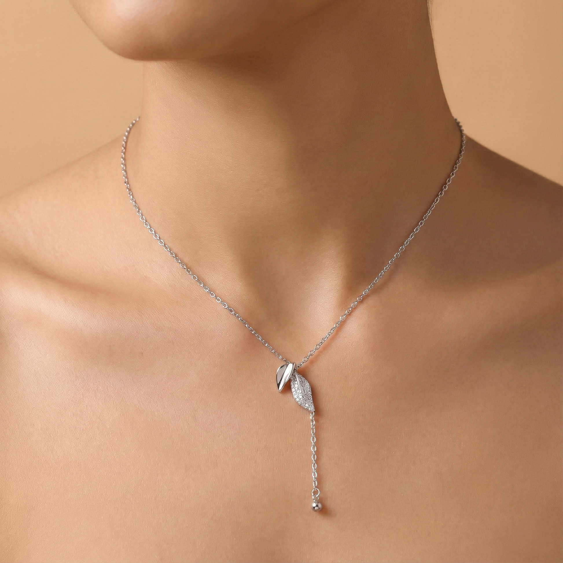 Silver necklace with a pendant on a person against a beige background
