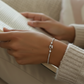 Close-up of a person's wrist wearing a silver bracelet with a neutral background