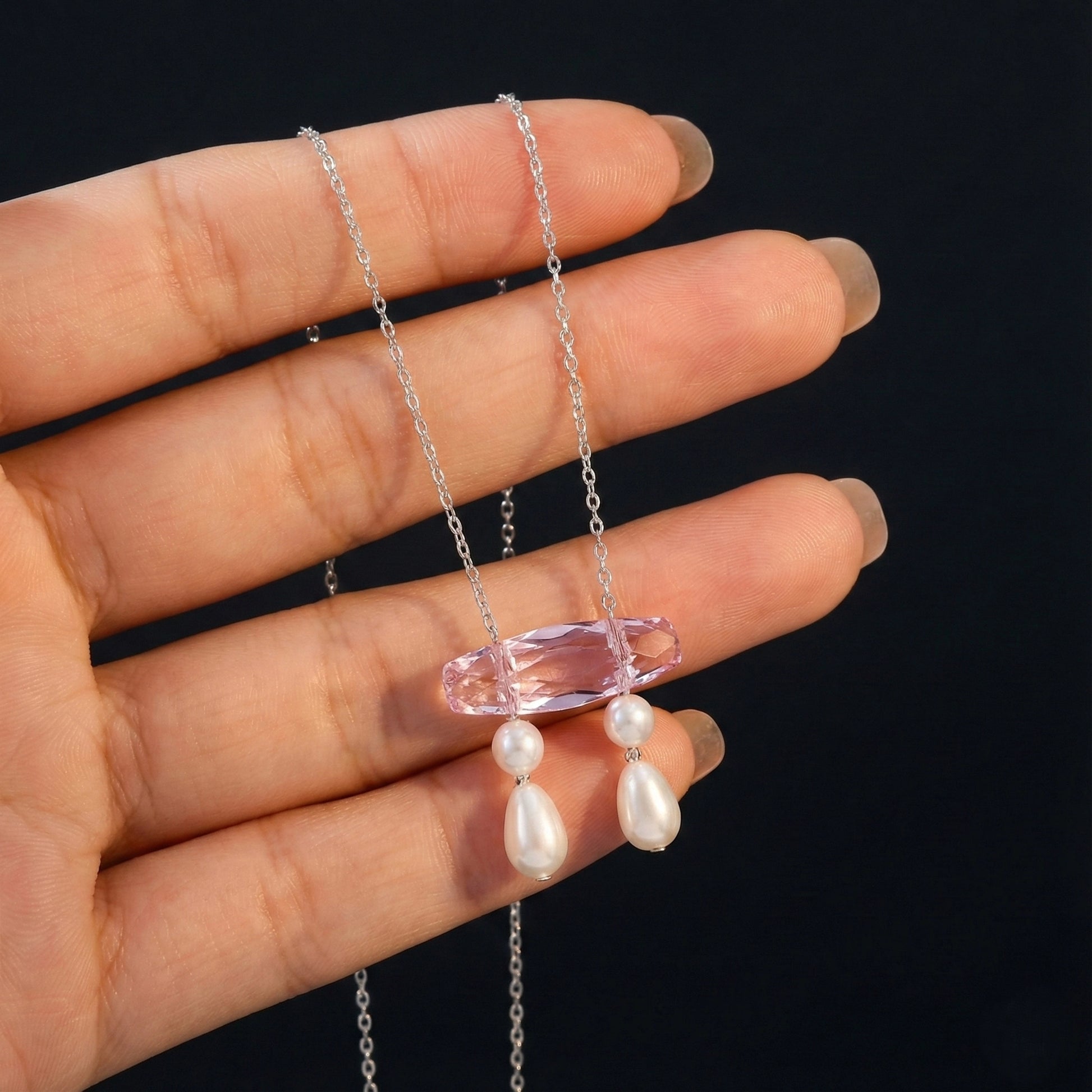 Necklace with pink pendant and pearl drops held by a hand against a black background