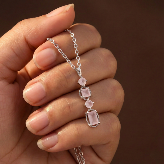 Hand holding a silver necklace with pink gemstones against a brown background