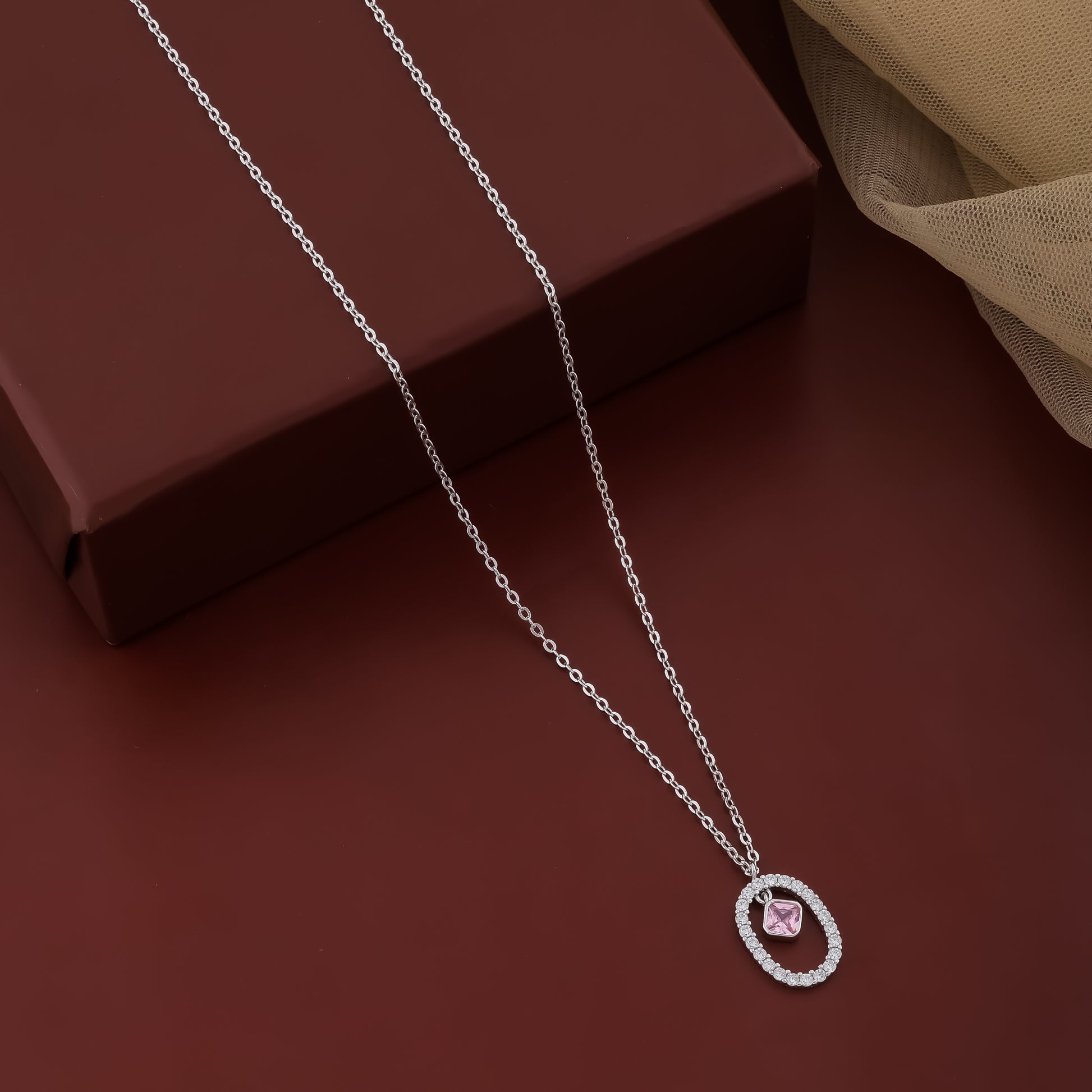 Silver necklace with a pink pendant on a brown surface