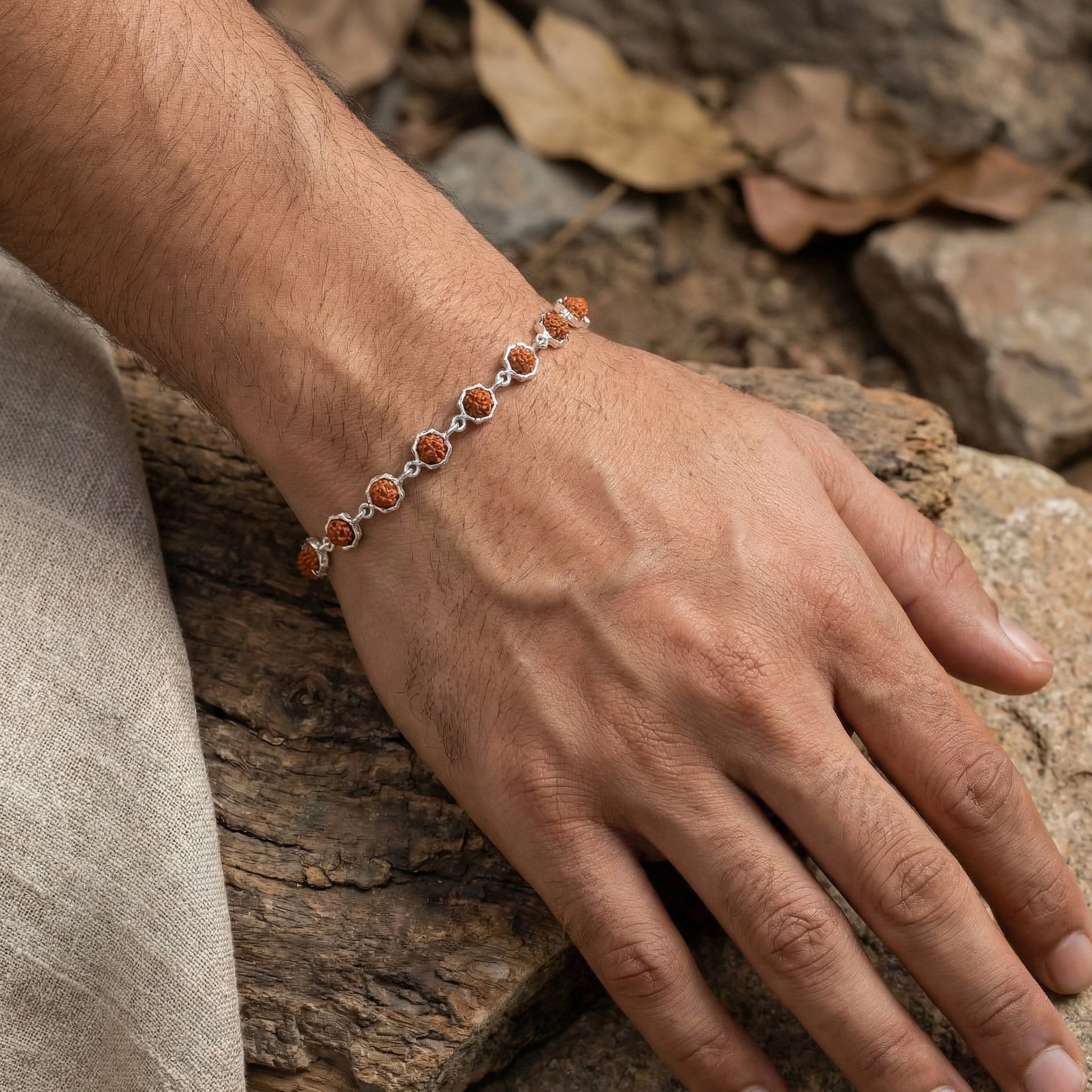 Hand wearing a bracelet with orange beads on a stone surface