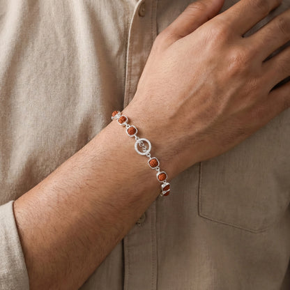 Close-up of a wrist wearing a bracelet with orange beads and a silver clasp, against a beige shirt background.