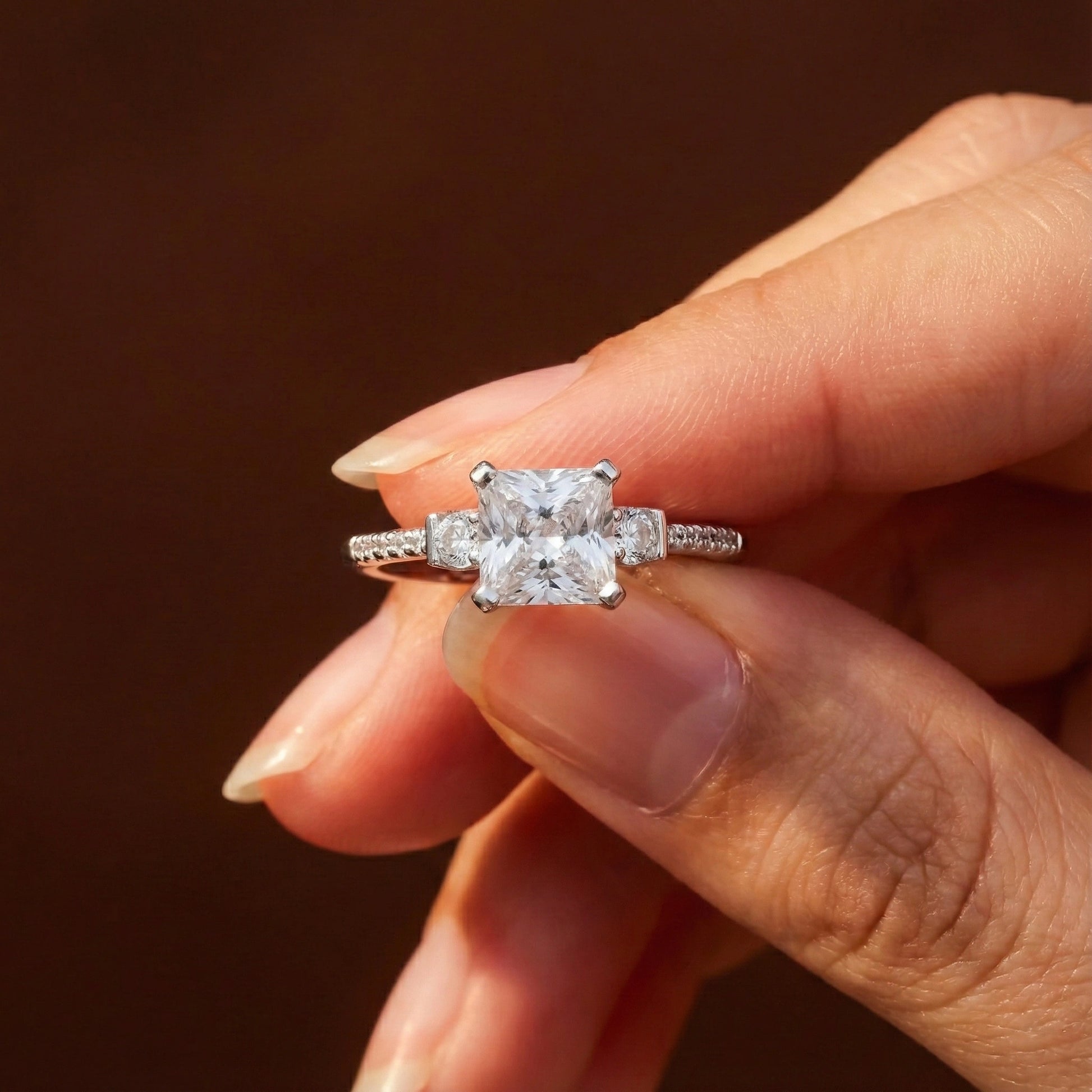 Diamond ring held between fingers against a dark background