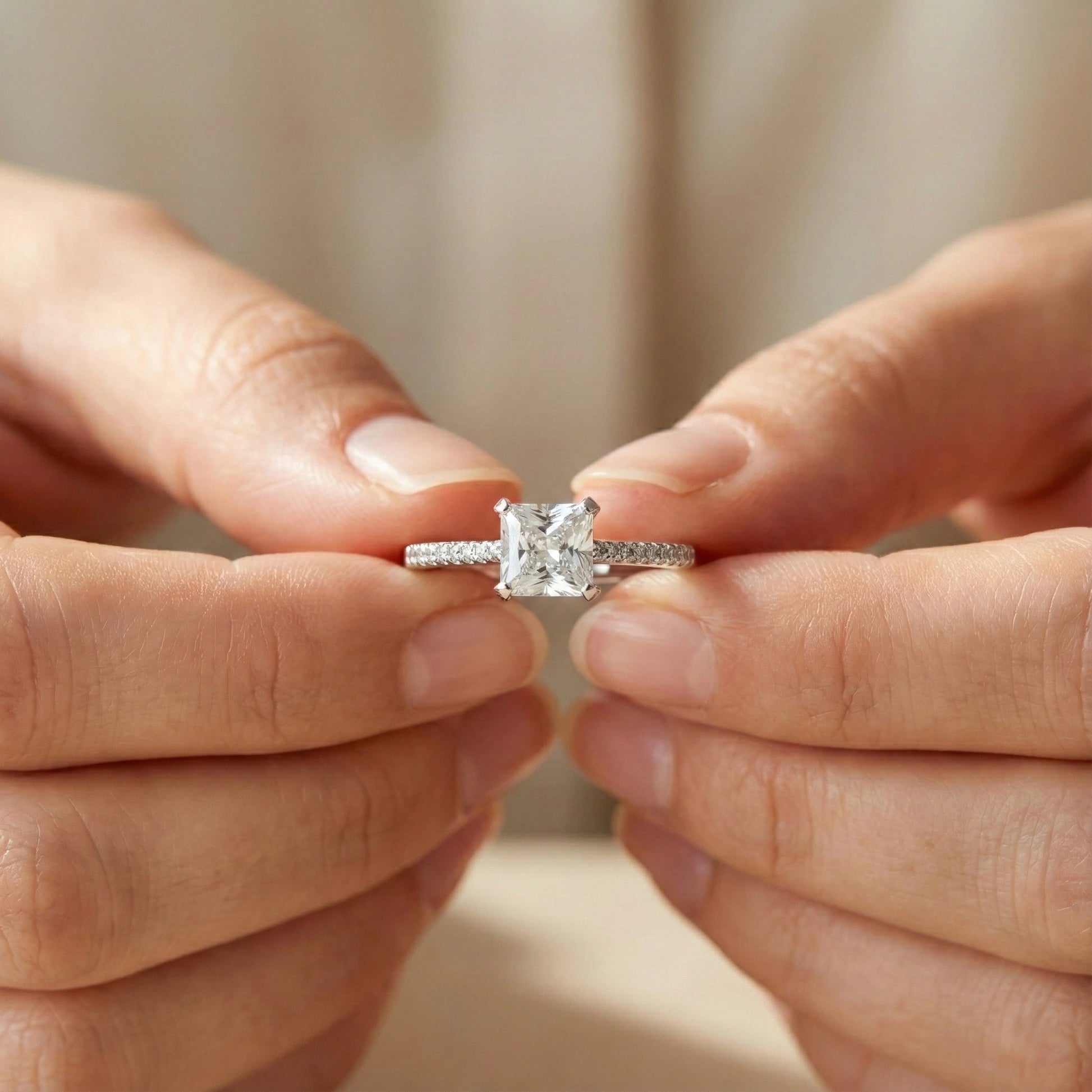 Diamond ring held between two hands against a neutral background