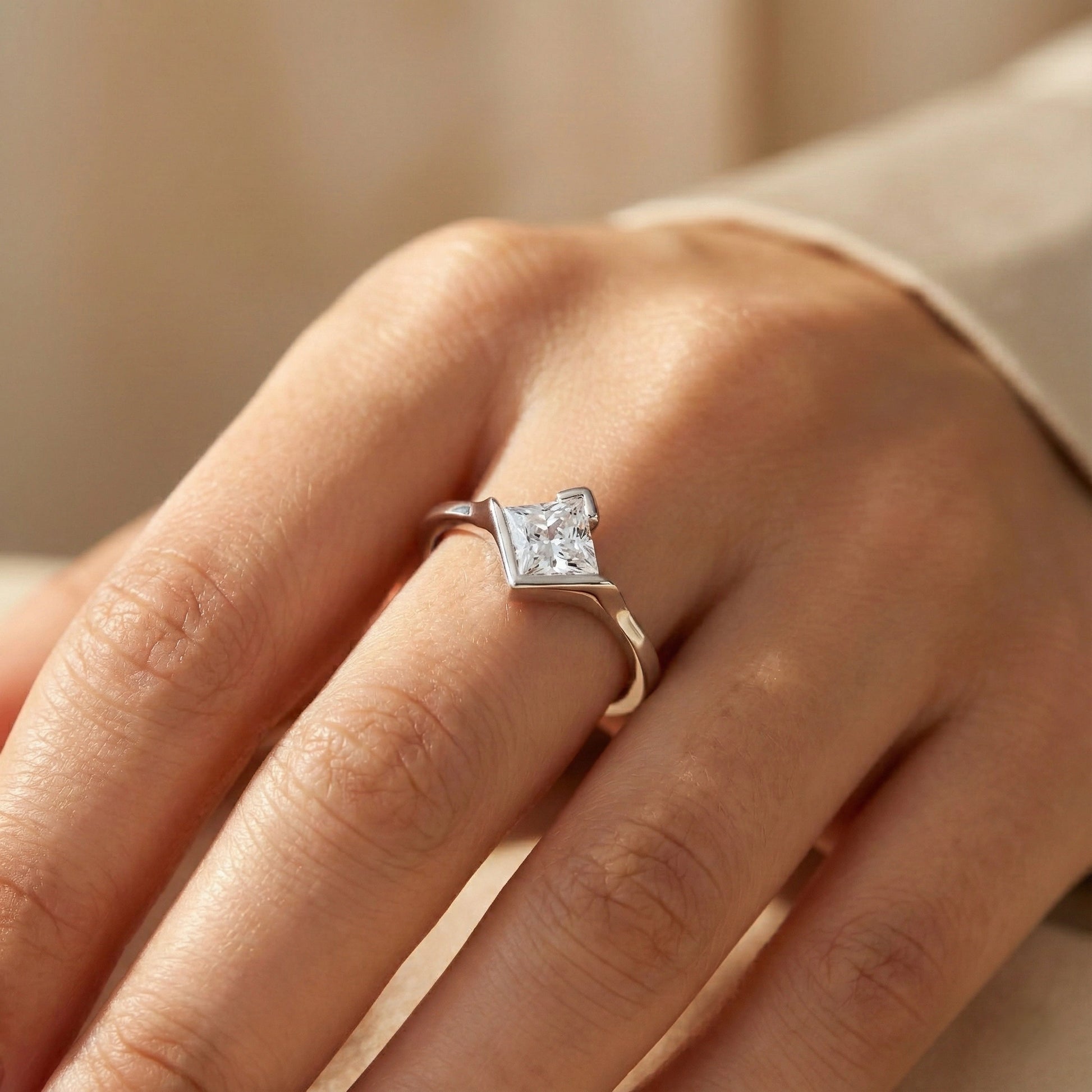Close-up of a hand wearing a diamond ring on a neutral background