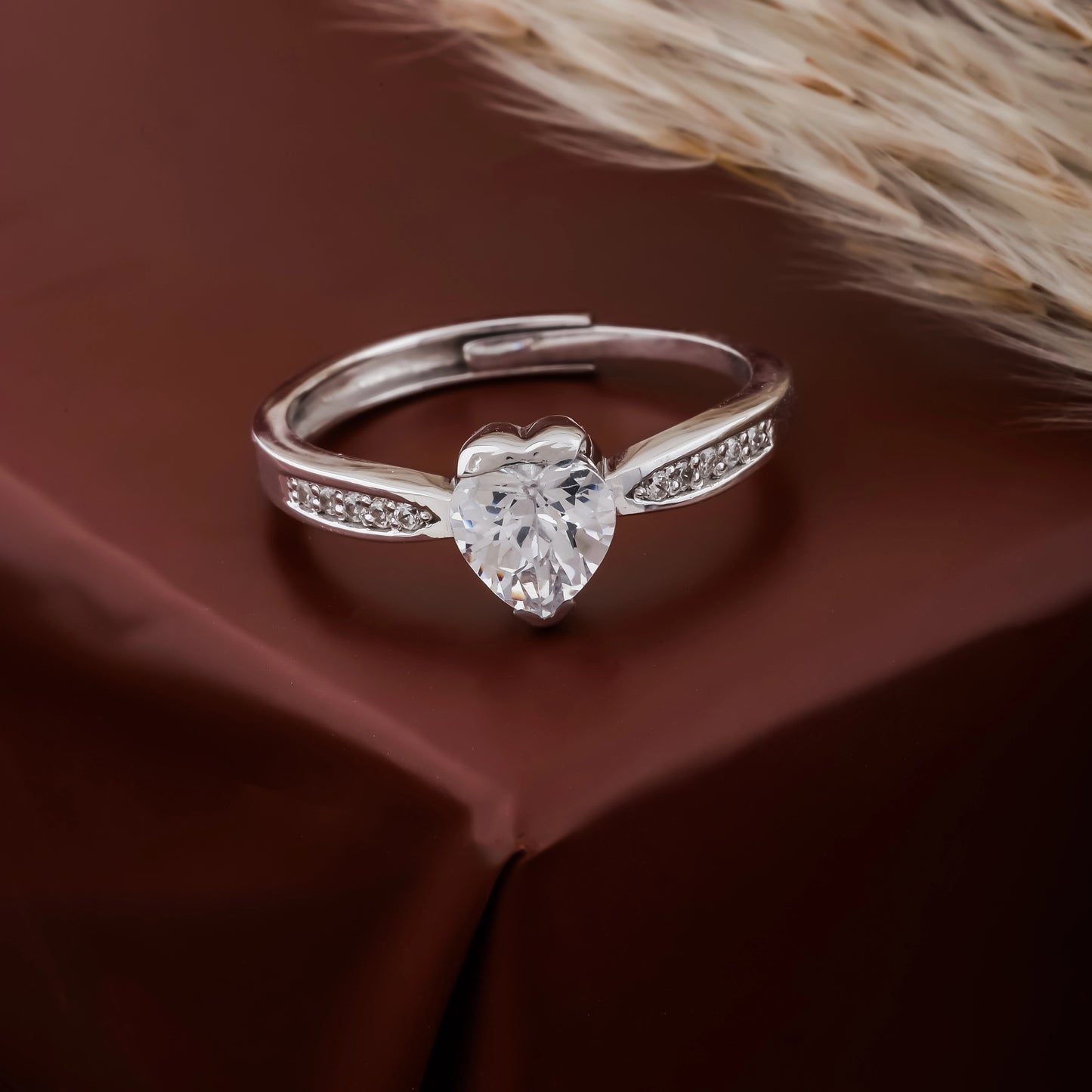Silver ring with a heart-shaped diamond on a brown fabric background