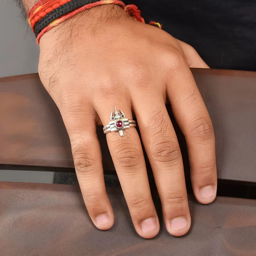 Hand wearing a silver ring with a red gemstone on a brown surface