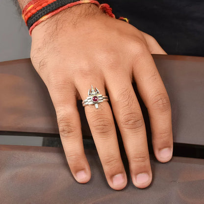 Hand wearing a silver ring with a red gemstone on a brown surface