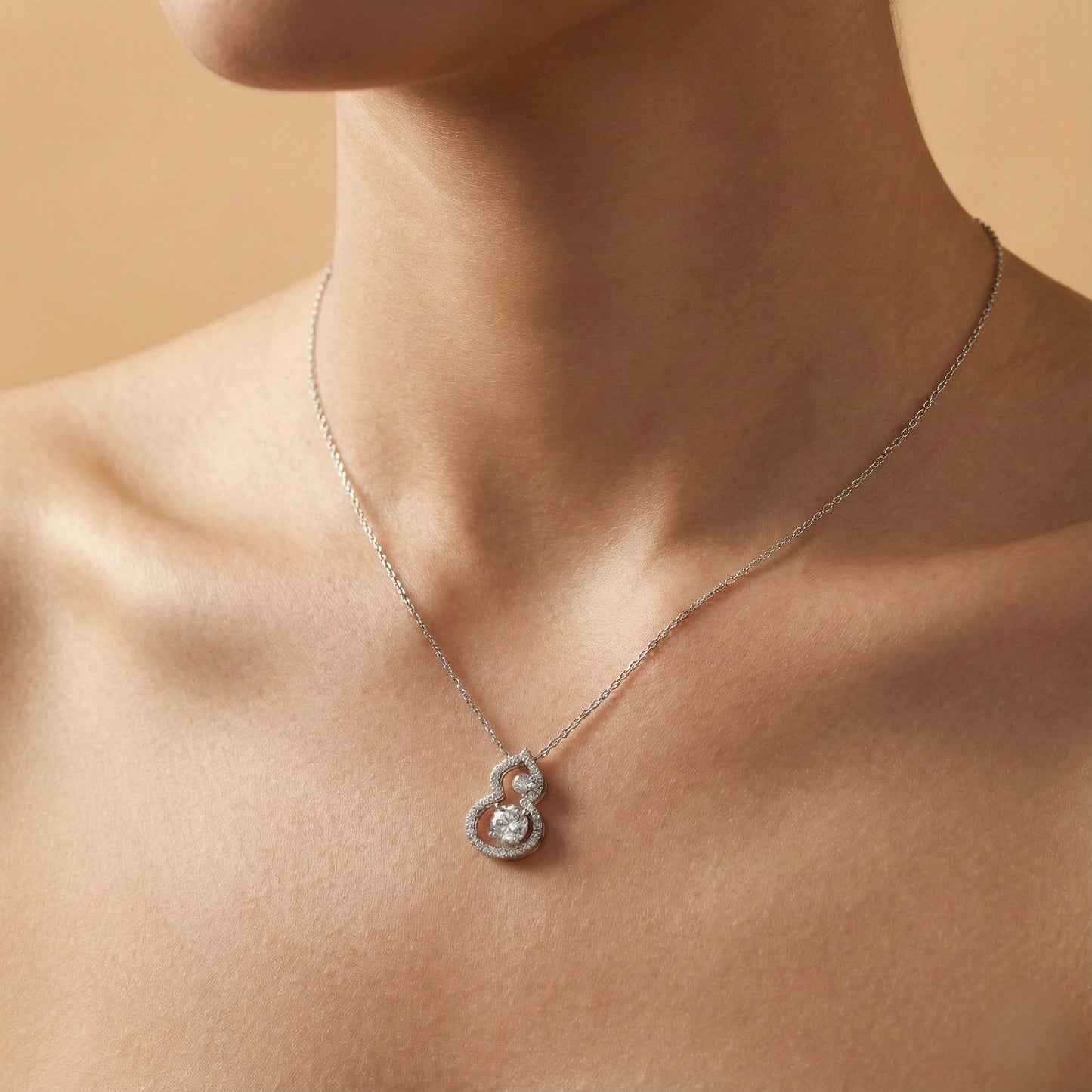 Silver necklace with a heart-shaped pendant on a person against a beige background
