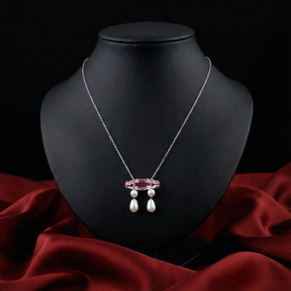Necklace with pink pendant and pearls on a black mannequin bust against a red fabric background