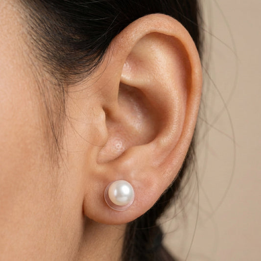Pair of white pearl stud earrings with smooth round finish placed on a brown background.