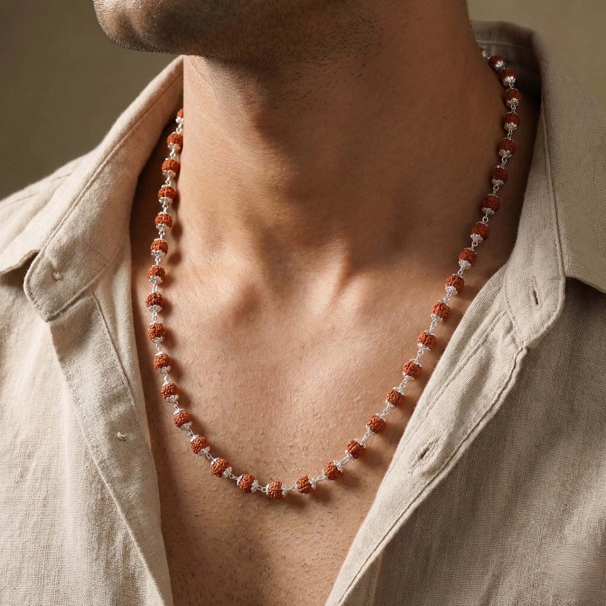 Rudraksha bead necklace with silver links displayed on beige background