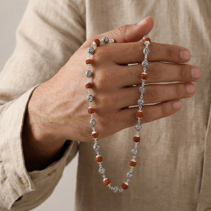 Hand holding a silver and red beaded necklace against a neutral background