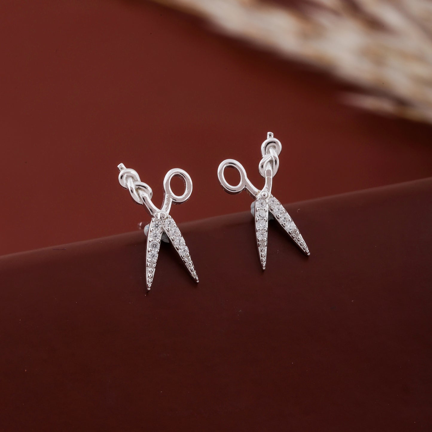 Silver scissors-shaped earrings on a brown surface