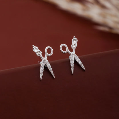 Silver scissors-shaped earrings on a brown surface