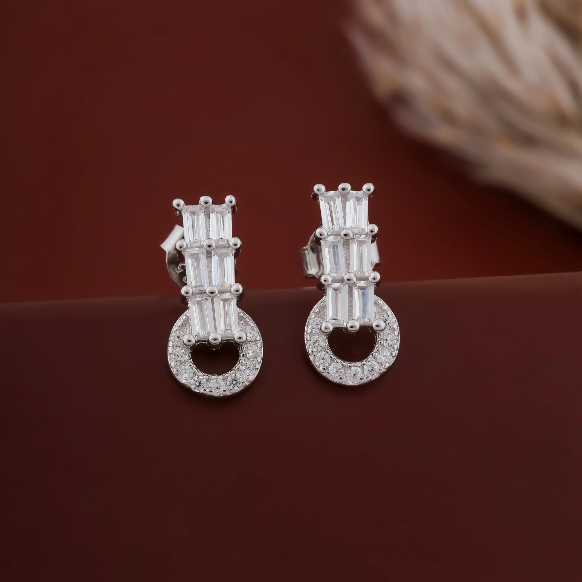 Pair of silver earrings with gemstones on a dark red background