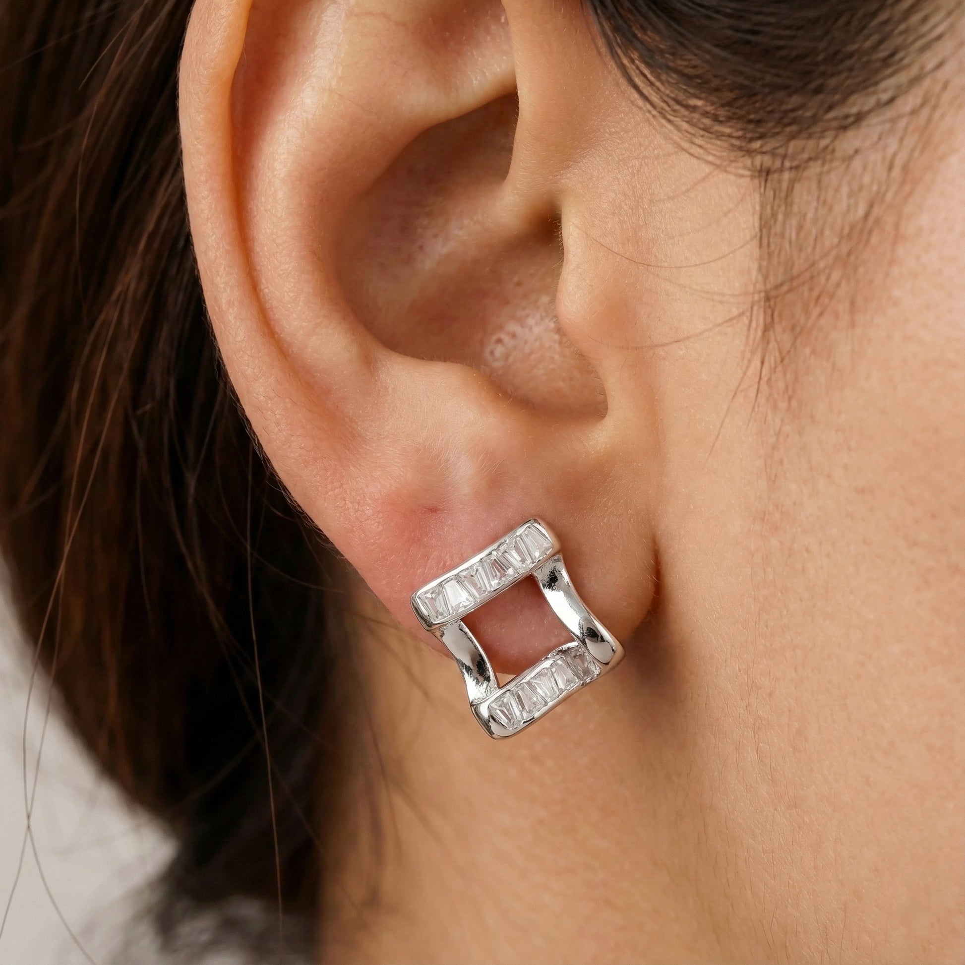 Silver square earring worn by a person