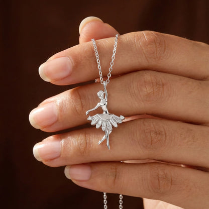 Silver ballerina pendant necklace held in a hand against a brown background