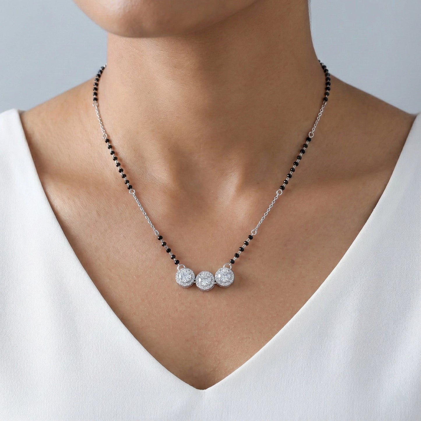 Necklace with black beads and silver pendants on a person wearing a white top.