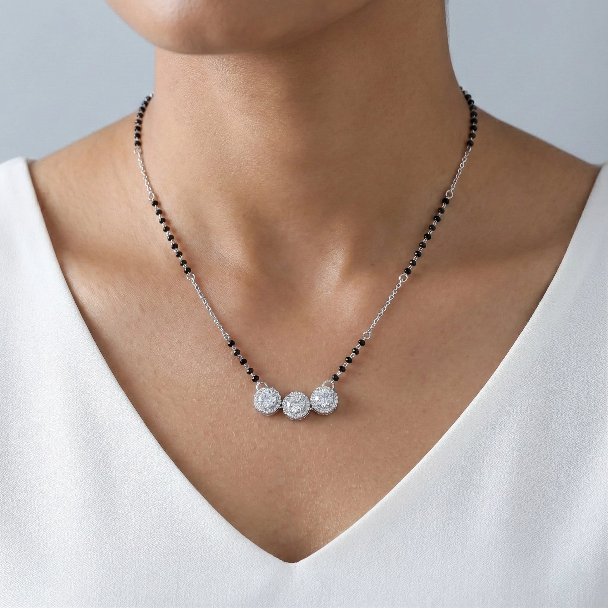 Necklace with black beads and silver pendants on a person wearing a white top.