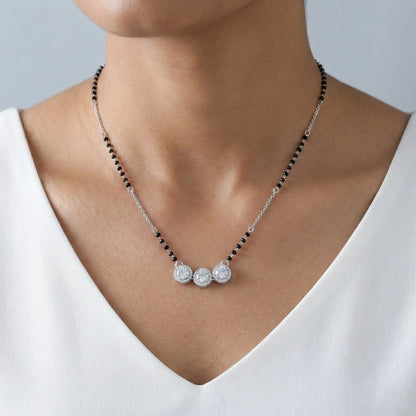 Necklace with black beads and silver pendants on a person wearing a white top.