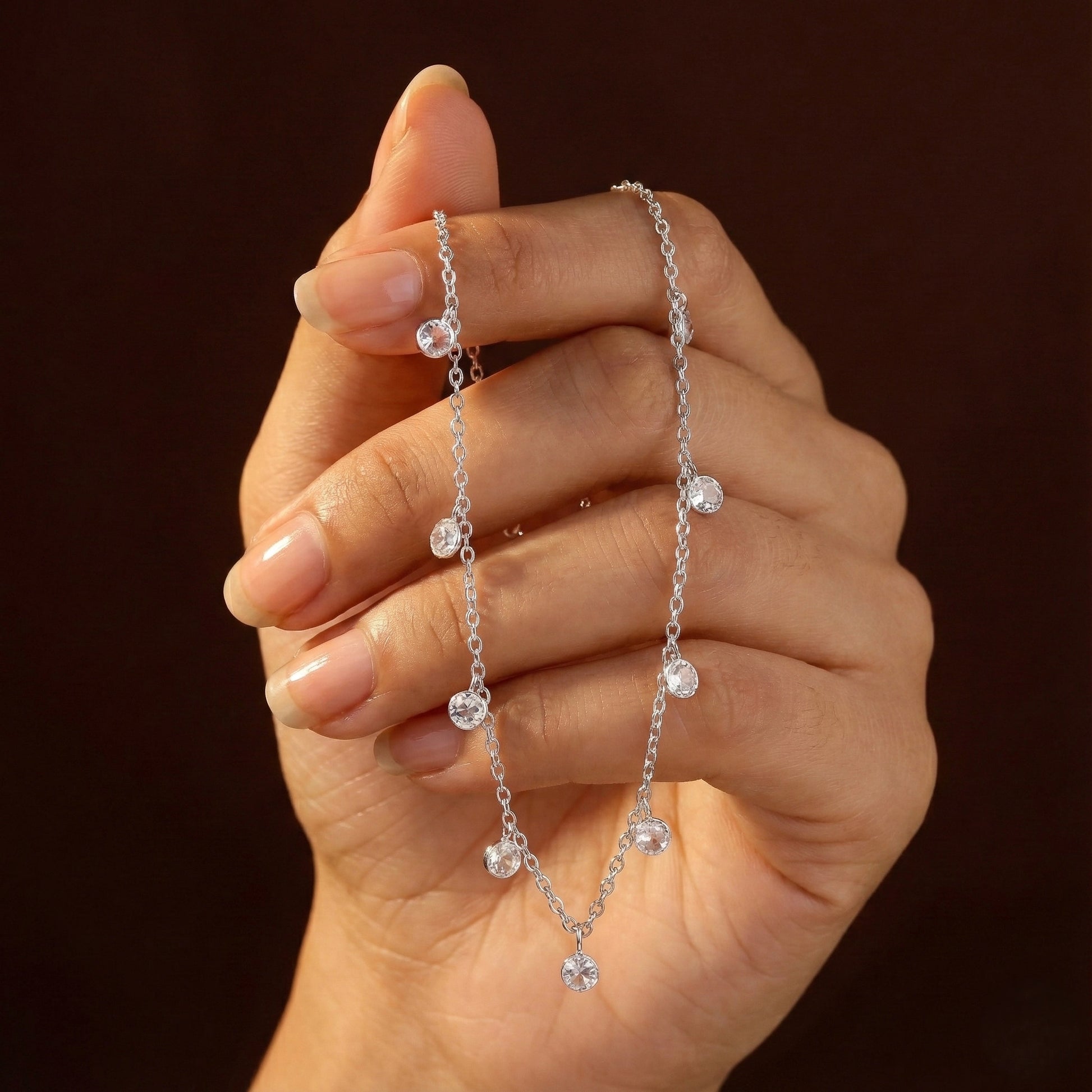 Hand holding a delicate silver necklace against a dark background