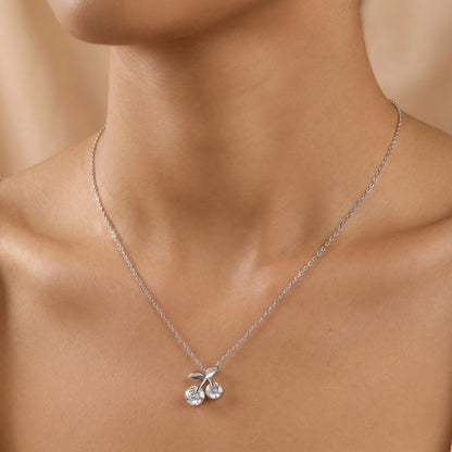 Silver necklace with a cherry pendant on a person's neck against a neutral background