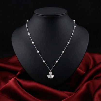 Pearl necklace with a shamrock pendant on a black mannequin bust against a dark background.