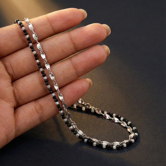 Hand holding a black beaded necklace with silver chain on a dark background