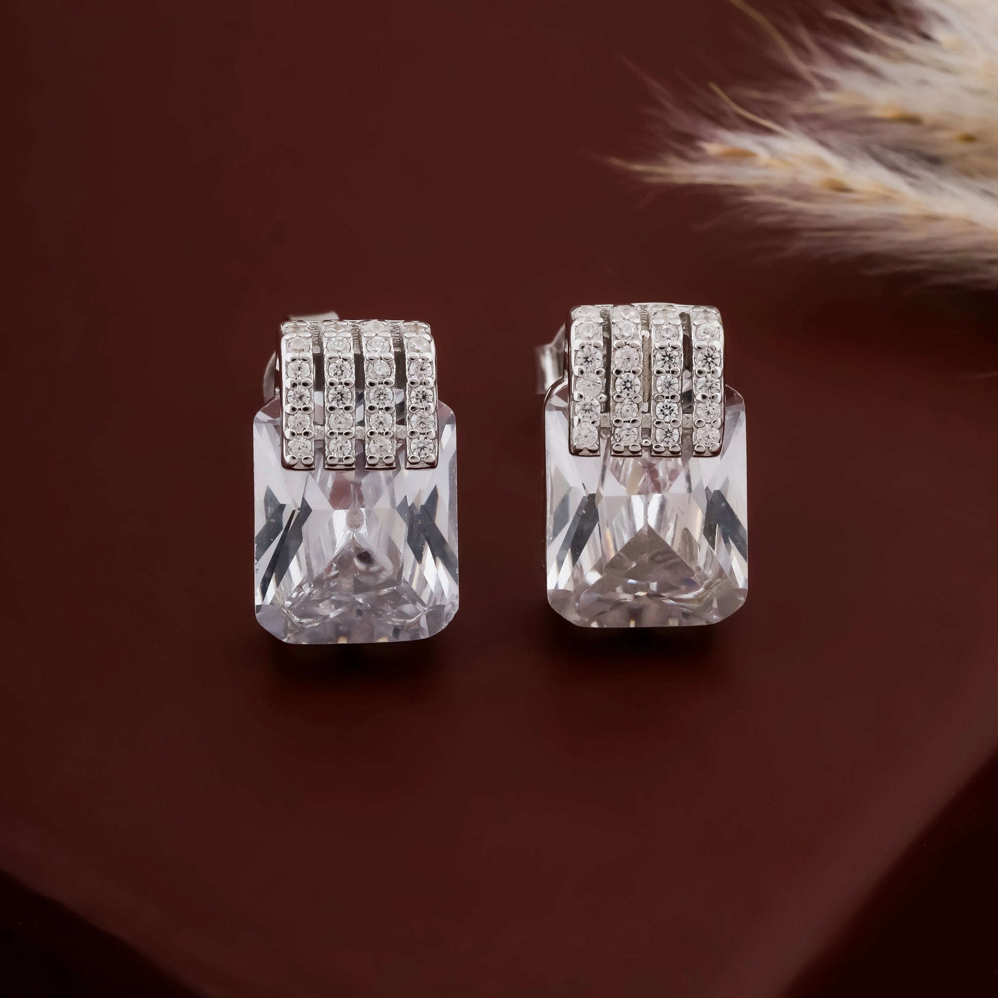 Pair of silver earrings with clear gemstones on a brown background