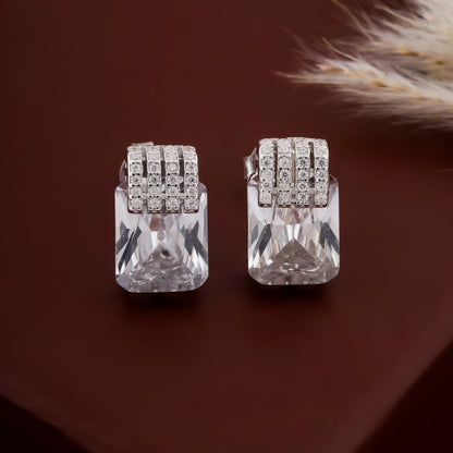 Pair of silver earrings with clear gemstones on a brown background