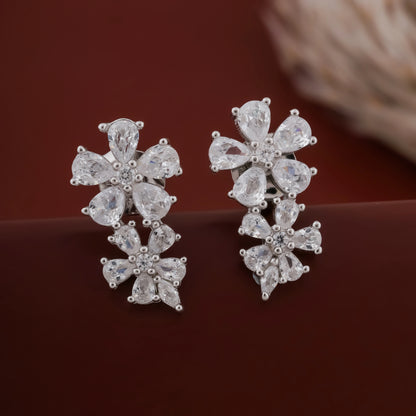 Pair of silver floral earrings on a dark brown background