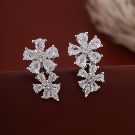 Pair of silver floral earrings on a dark brown background