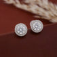 Pair of diamond earrings on a brown surface with blurred natural background