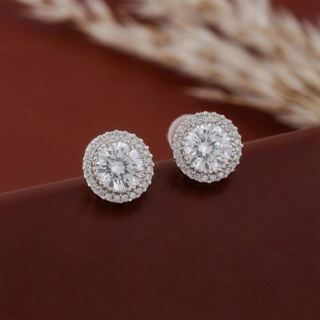 Pair of diamond earrings on a brown surface with blurred natural background