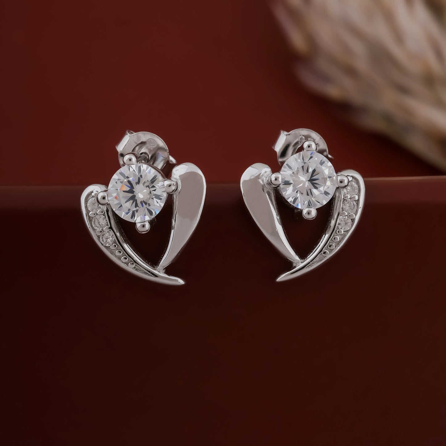 Silver heart-shaped earrings with clear gemstones on a dark background