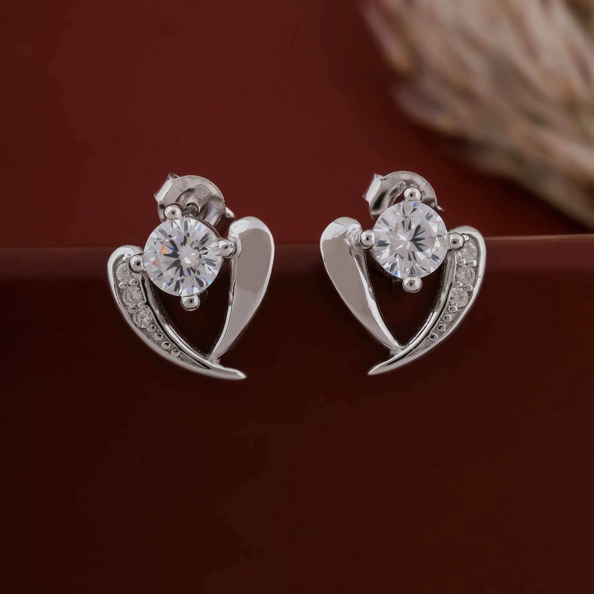 Silver heart-shaped earrings with clear gemstones on a dark background