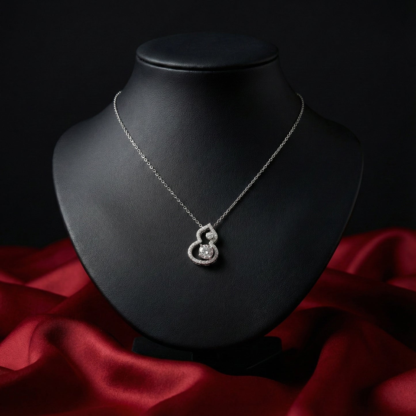 Silver necklace with a heart-shaped pendant on a black mannequin bust against a red fabric background