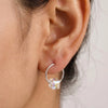 Close-up of an ear wearing a silver hoop earring with a clear gemstone.