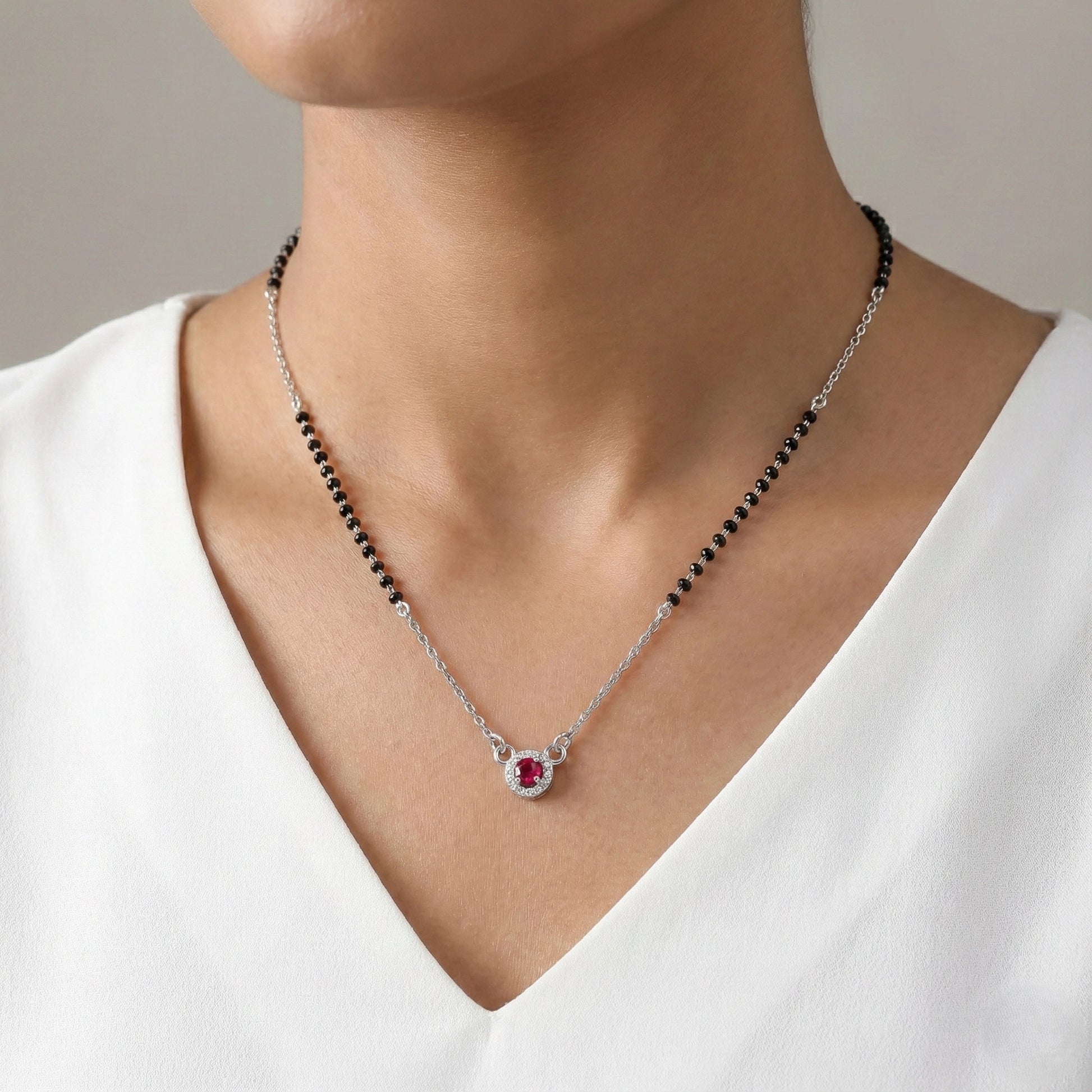 Necklace with a red gemstone pendant worn by a person in a white top.