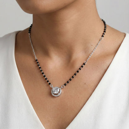 Necklace with black beads and a silver pendant on a person wearing a white top.