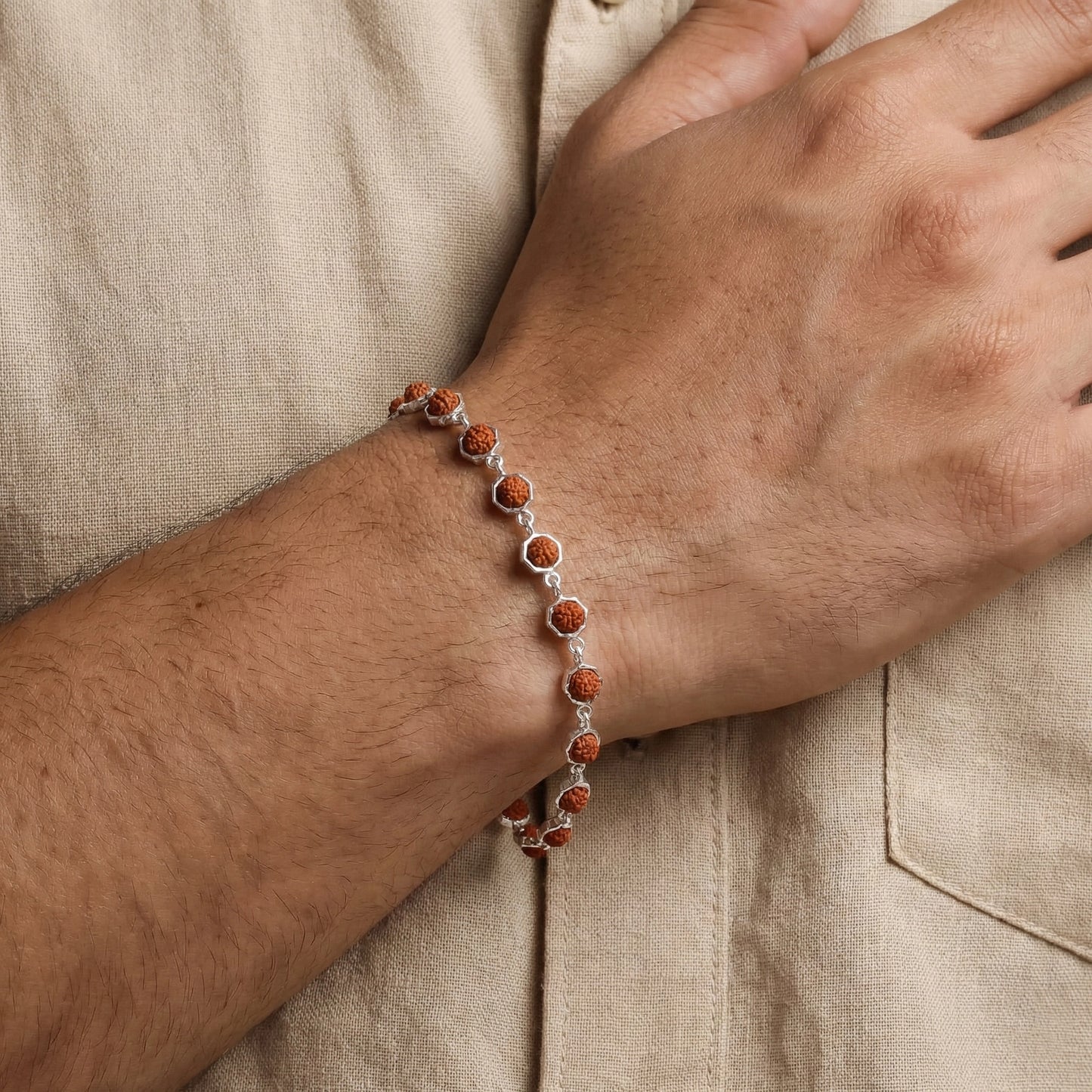 Close-up of a wrist wearing a bracelet with red stones on a beige fabric background