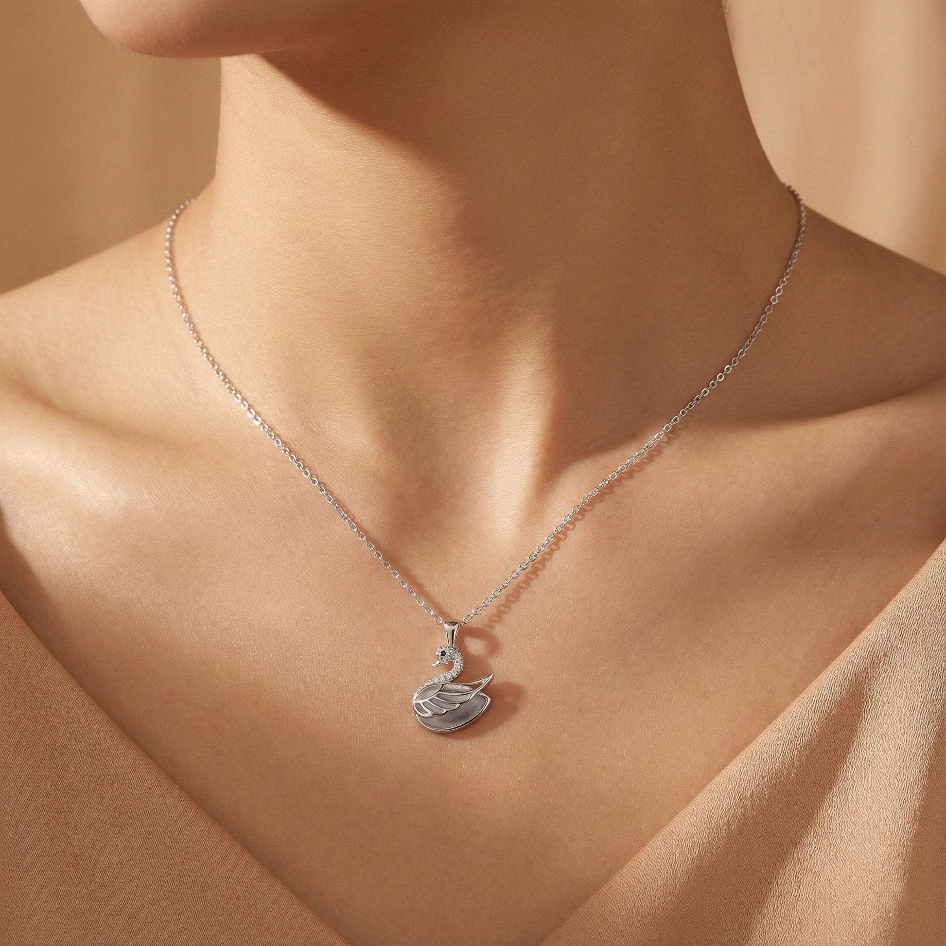 Silver swan pendant necklace on a person's neck against a neutral background