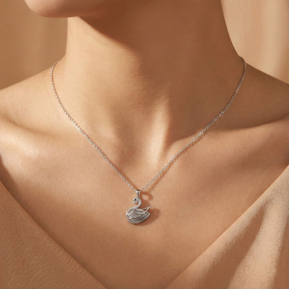 Silver swan pendant necklace on a person's neck against a neutral background